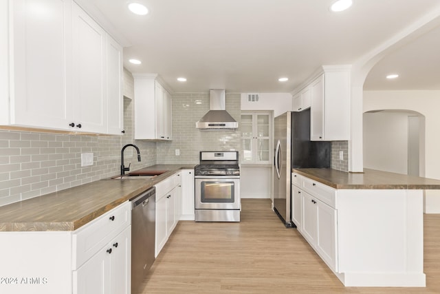 kitchen with wall chimney range hood, appliances with stainless steel finishes, light wood-type flooring, and white cabinetry