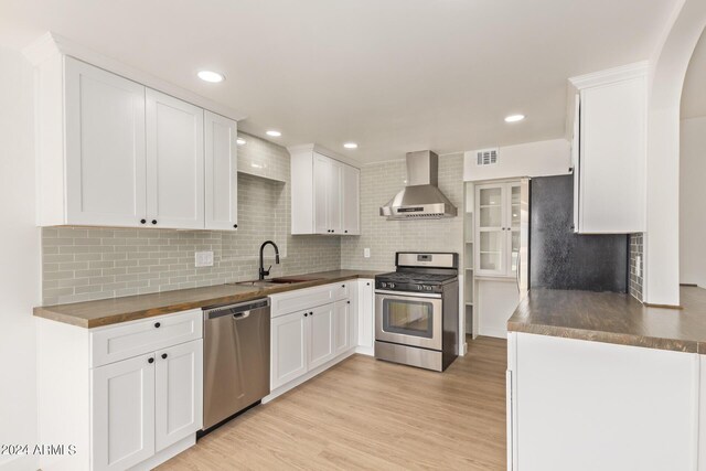 kitchen with white cabinetry, stainless steel appliances, wood counters, sink, and wall chimney exhaust hood