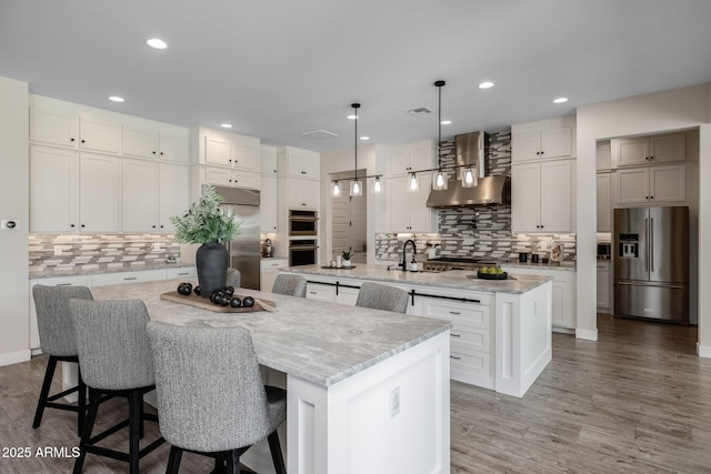 kitchen with a large island, wall chimney range hood, a breakfast bar area, and stainless steel appliances