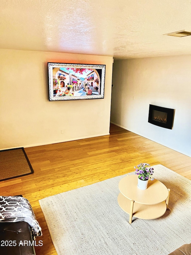 living room with a glass covered fireplace, visible vents, baseboards, and wood finished floors