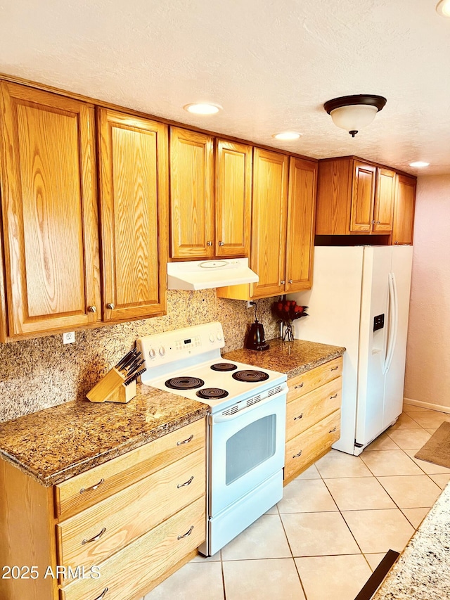 kitchen with tasteful backsplash, light stone counters, white appliances, light tile patterned floors, and under cabinet range hood