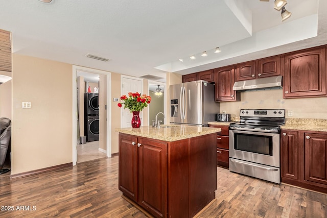 50031 N 27th Ave, New River, AZ 85087 - kitchen featuring appliances with stainless steel finishes, under cabinet range hood, wood finished floors, stacked washer and clothes dryer, and a center island with sink