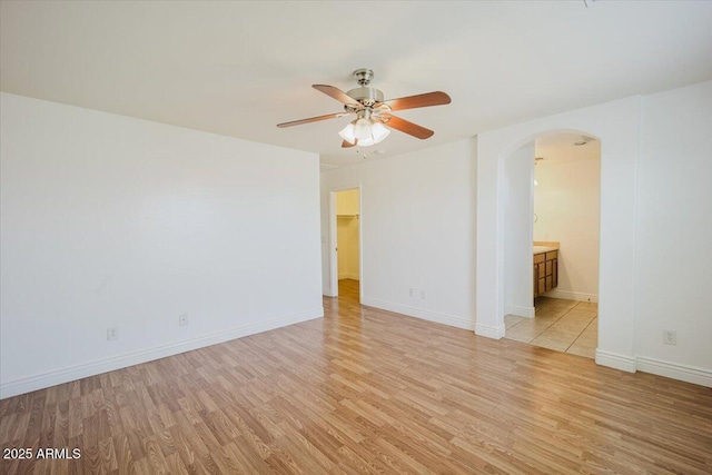empty room with arched walkways, light wood-style floors, baseboards, and a ceiling fan