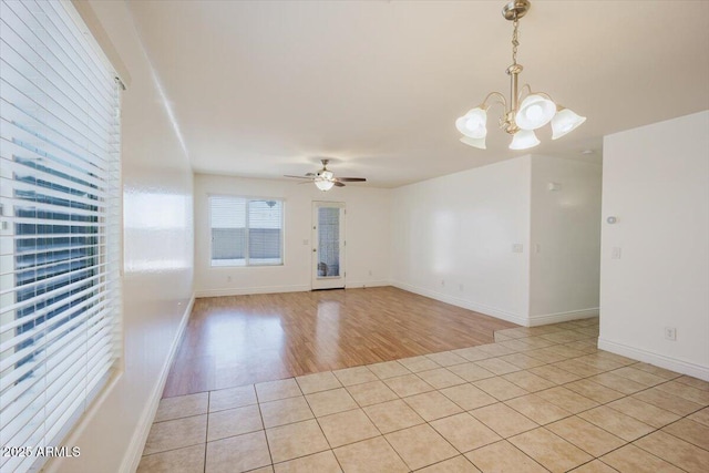 empty room with ceiling fan with notable chandelier, light tile patterned flooring, and baseboards