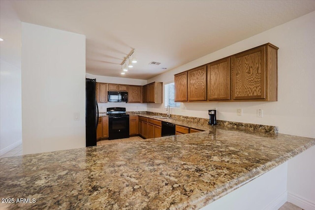 kitchen featuring track lighting, dark stone countertops, black appliances, visible vents, and a sink