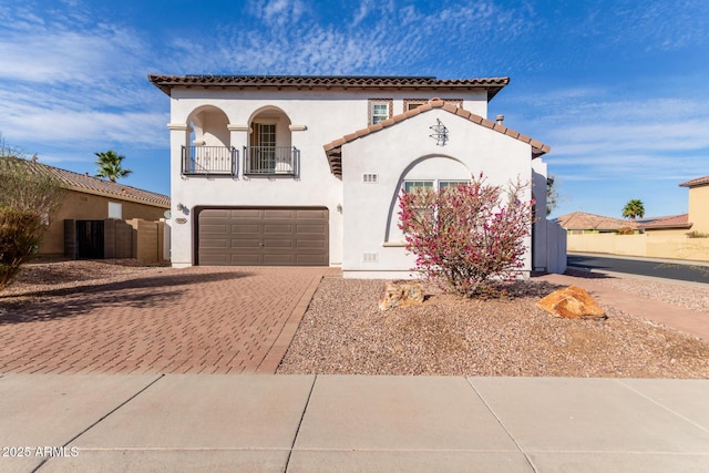 mediterranean / spanish-style house featuring a balcony, a garage, decorative driveway, and stucco siding