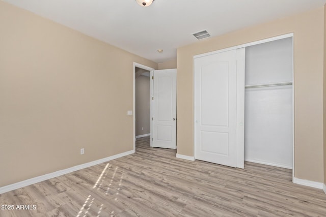 unfurnished bedroom featuring light wood-type flooring, baseboards, visible vents, and a closet