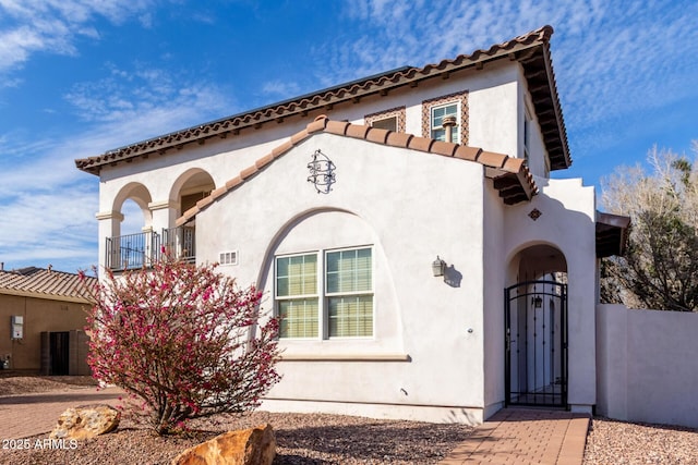 mediterranean / spanish-style house featuring a tile roof, stucco siding, a gate, fence, and a balcony