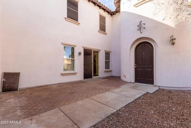 view of exterior entry with a patio area, a tile roof, and stucco siding