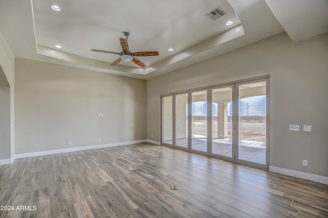 unfurnished room with ceiling fan, hardwood / wood-style floors, and a tray ceiling