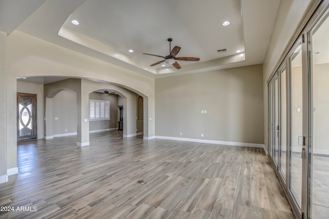 unfurnished living room with ceiling fan, light hardwood / wood-style flooring, and a raised ceiling