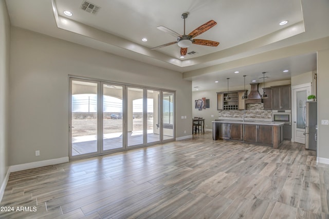 kitchen featuring a kitchen island, a raised ceiling, custom exhaust hood, decorative backsplash, and stainless steel appliances