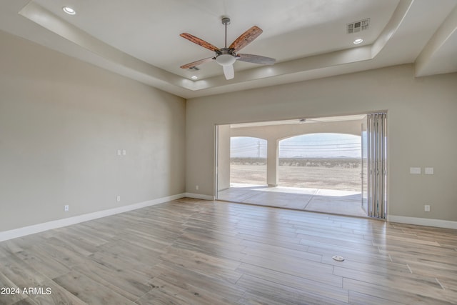 unfurnished room with ceiling fan, a tray ceiling, and light hardwood / wood-style flooring