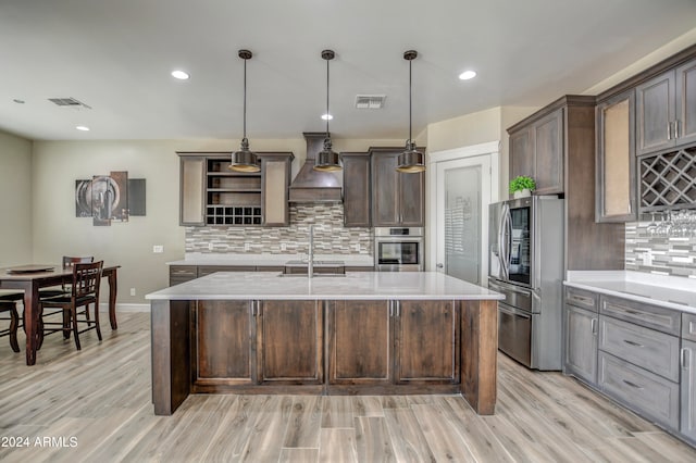 kitchen featuring custom exhaust hood, decorative backsplash, hanging light fixtures, a kitchen island with sink, and appliances with stainless steel finishes