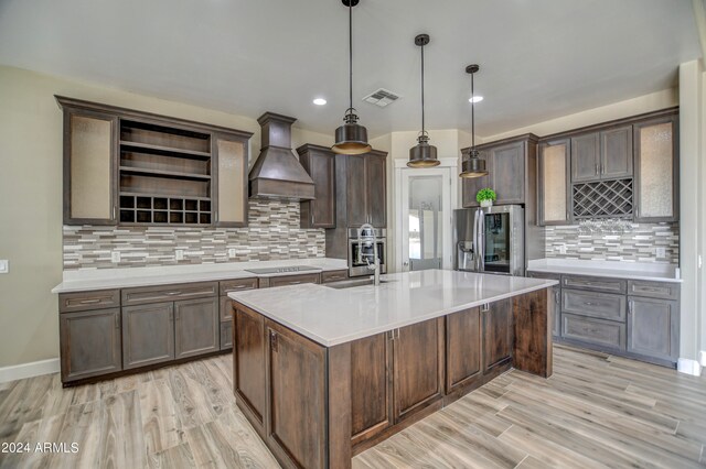 kitchen with premium range hood, stainless steel appliances, decorative light fixtures, dark brown cabinetry, and sink