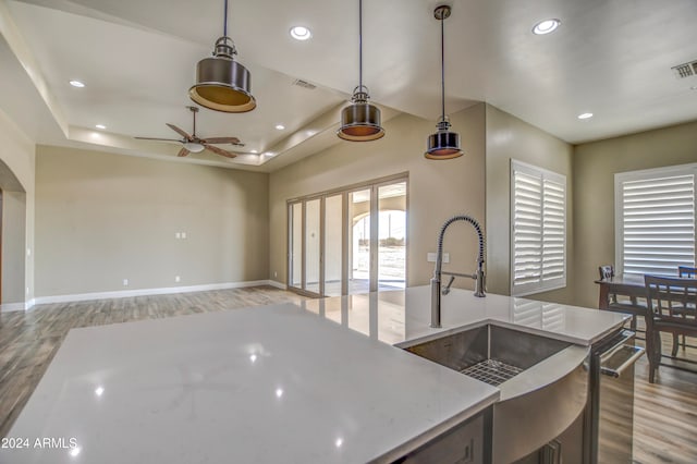 kitchen with ceiling fan, pendant lighting, a raised ceiling, sink, and light wood-type flooring