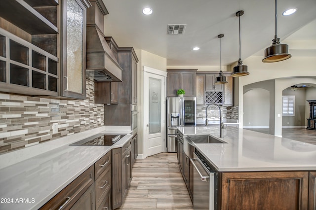 kitchen featuring sink, hanging light fixtures, custom range hood, and an island with sink