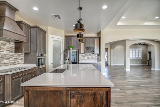 kitchen featuring a center island with sink, ceiling fan, appliances with stainless steel finishes, custom range hood, and pendant lighting