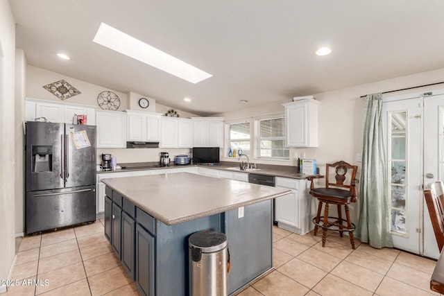 kitchen featuring vaulted ceiling with skylight, white cabinets, a center island, stainless steel appliances, and light tile patterned floors