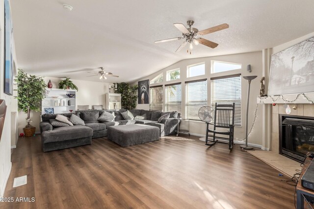 living room with a textured ceiling, dark hardwood / wood-style flooring, vaulted ceiling, ceiling fan, and a tile fireplace