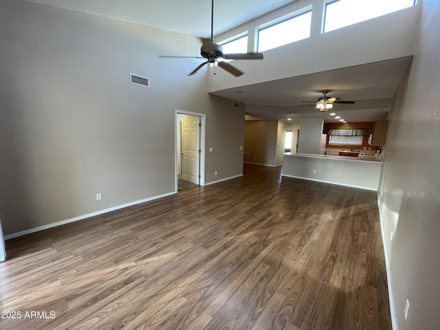 unfurnished living room with a high ceiling, ceiling fan, and dark hardwood / wood-style flooring