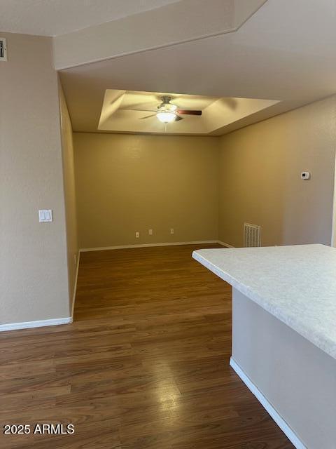 empty room with ceiling fan, dark hardwood / wood-style flooring, and a tray ceiling