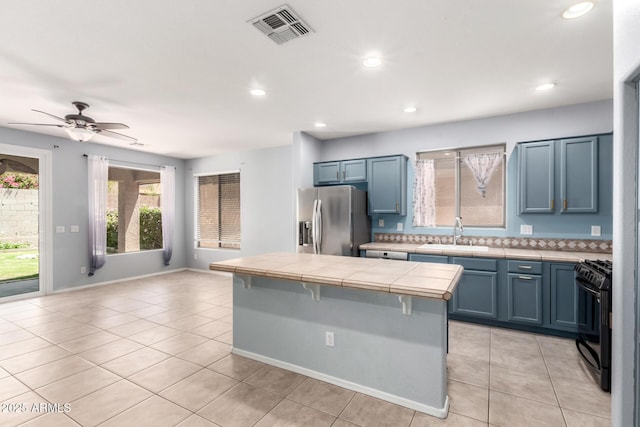 9142 W Pontiac Dr, Peoria, AZ 85382 - kitchen with stainless steel fridge with ice dispenser, black gas range, tile counters, light tile patterned floors, and a center island