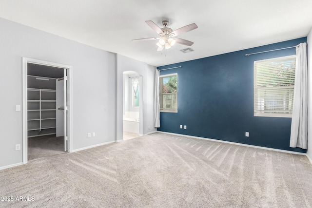 9142 W Pontiac Dr, Peoria, AZ 85382 - unfurnished bedroom featuring arched walkways, carpet, a walk in closet, a ceiling fan, and ensuite bathroom
