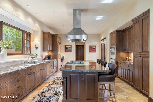 kitchen featuring island range hood, a kitchen island, a sink, a kitchen breakfast bar, and dark stone countertops