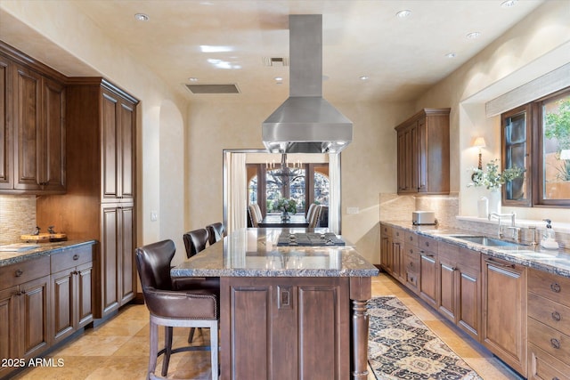 kitchen featuring a center island, a breakfast bar, stone countertops, a sink, and island range hood