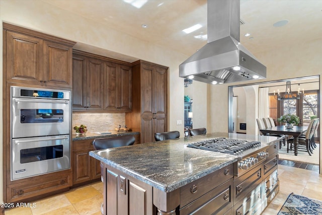 kitchen featuring a kitchen island, appliances with stainless steel finishes, dark stone counters, tasteful backsplash, and island exhaust hood