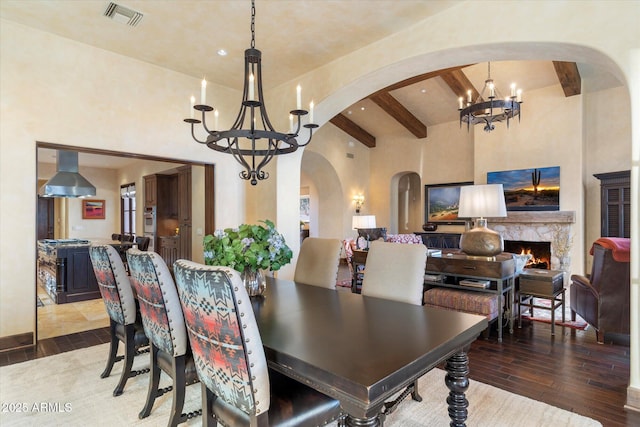 dining area with beam ceiling, visible vents, a premium fireplace, wood finished floors, and a chandelier