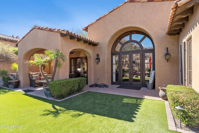 doorway to property with a lawn, a patio, a tiled roof, french doors, and stucco siding