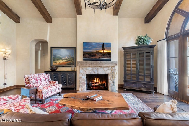 living room with baseboards, arched walkways, beamed ceiling, wood finished floors, and a stone fireplace