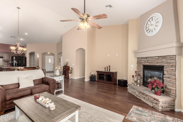 living room with ceiling fan with notable chandelier, a fireplace, high vaulted ceiling, and dark wood-type flooring