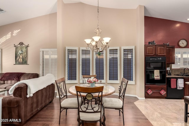 dining space featuring sink, high vaulted ceiling, light wood-type flooring, and a notable chandelier