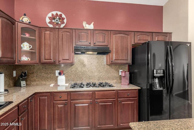 kitchen featuring decorative backsplash, black fridge with ice dispenser, light stone countertops, and stainless steel gas cooktop