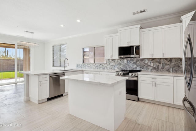 kitchen with stainless steel appliances, a kitchen island, sink, and white cabinets