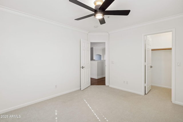 unfurnished bedroom featuring crown molding, a walk in closet, light carpet, and ceiling fan