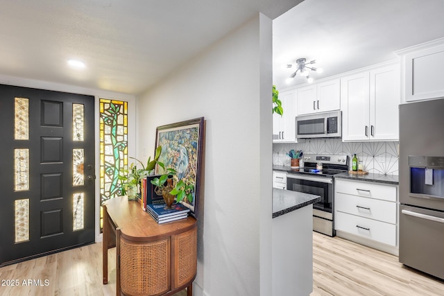 kitchen featuring stainless steel appliances, light wood-style flooring, backsplash, and white cabinetry