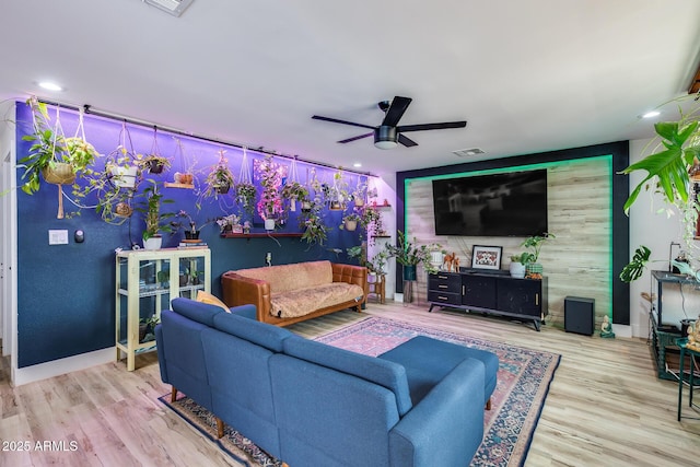 living room featuring baseboards, visible vents, a ceiling fan, an accent wall, and wood finished floors