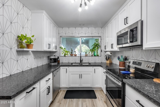 kitchen featuring tasteful backsplash, white cabinets, light wood-style flooring, appliances with stainless steel finishes, and a sink