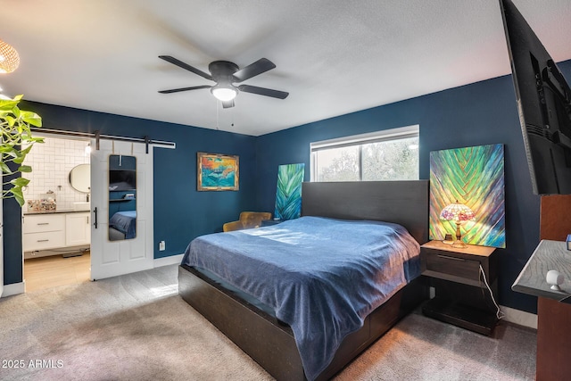 bedroom featuring baseboards, a barn door, ensuite bath, and light colored carpet