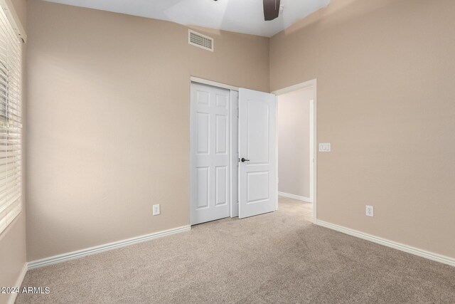 unfurnished bedroom featuring vaulted ceiling, light colored carpet, a closet, and ceiling fan