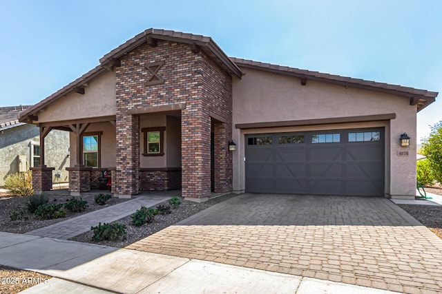 view of front of property with a garage, brick siding, a tiled roof, decorative driveway, and stucco siding