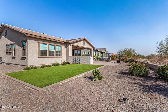 back of property featuring a lawn, a patio area, and stucco siding