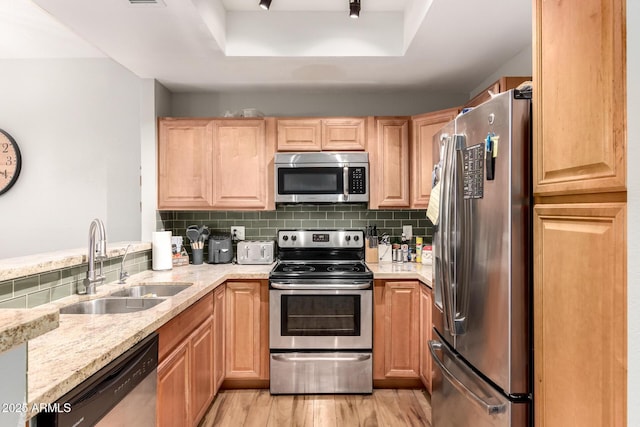 kitchen with appliances with stainless steel finishes, sink, backsplash, light wood-type flooring, and a tray ceiling