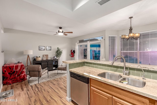 kitchen with sink, hanging light fixtures, light wood-type flooring, light stone counters, and stainless steel dishwasher