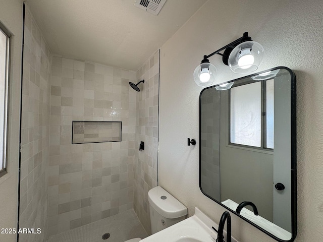 bathroom with sink, a tile shower, and toilet