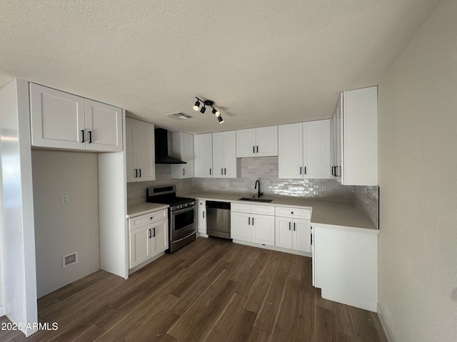 kitchen with dark wood-type flooring, wall chimney exhaust hood, sink, stainless steel appliances, and white cabinets